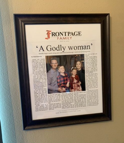 Personalized newspaper story titled 'A Godly Woman' hanging on the wall in a frame