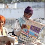 two older people reading the newspaper outside