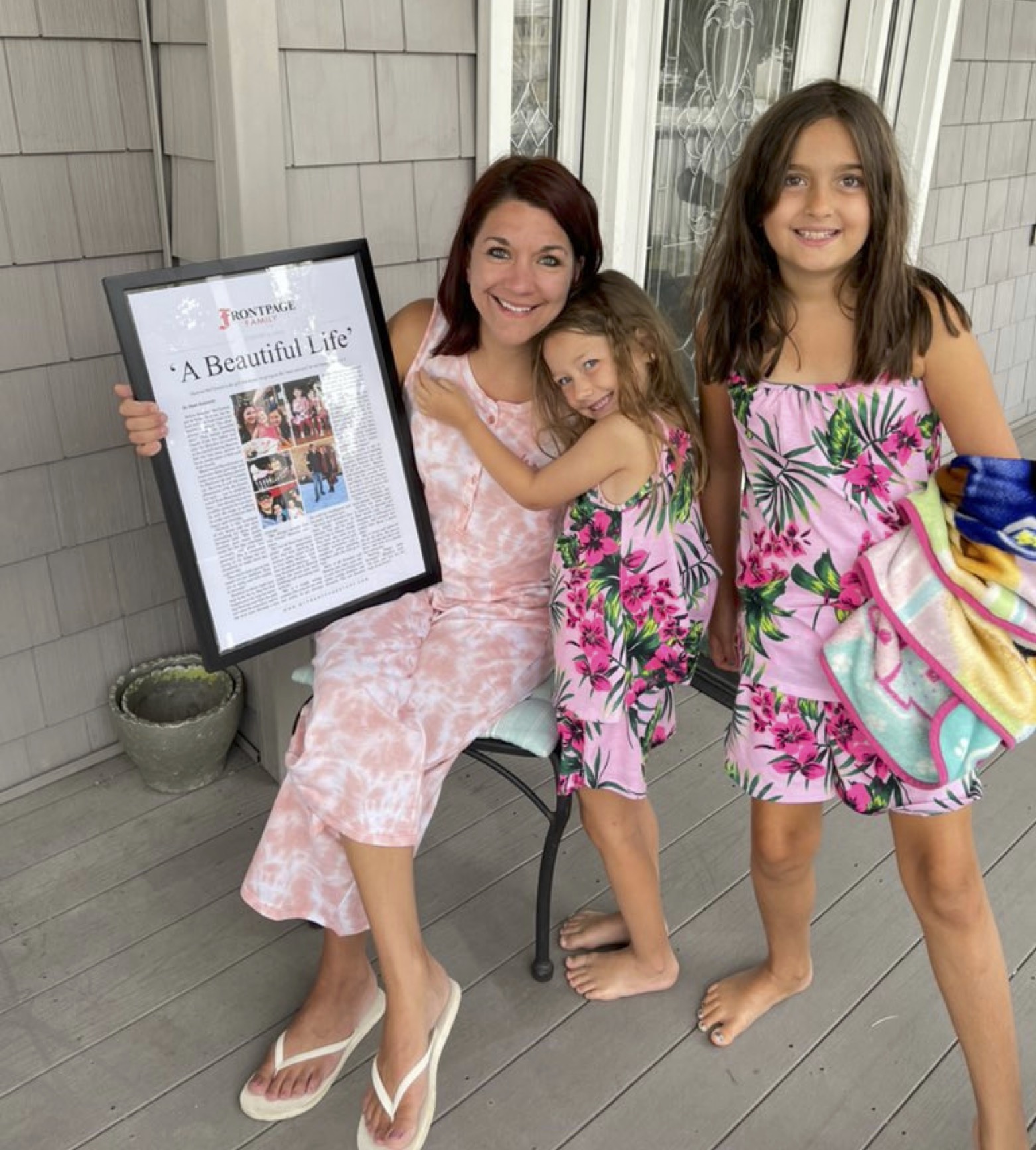 Mom smiling with personalized newspaper story and daughters (plus)
