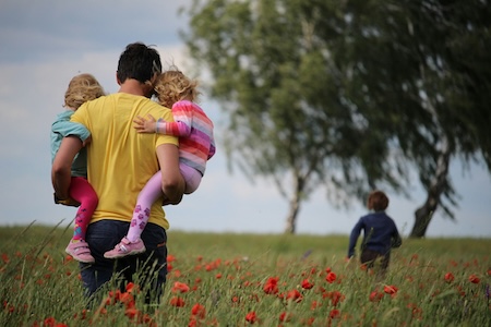 father holding his two daughters in a field - happy (early) Father's Day