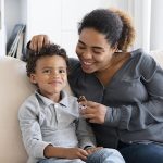 A mom smiling on the couch with her son feeding him a chocolate bar - raising a little leader