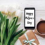 for unforgettable Mother's Day gifts blog post | happy mothers day text sign on stylish gift and phone and tulips and coffee on white wooden rustic background. flat lay with flowers and gadget with empty screen with space for text.