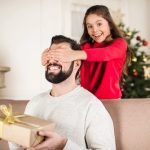 Christmas gift for dad blog post - smiling daughter covering father eyes from back