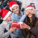 Christmas gifts for Mom blog post - daughter closing Mom's eyes while son is handing her a Christmas gift